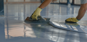 Technician installing epoxy garage flooring while wearing gloves.