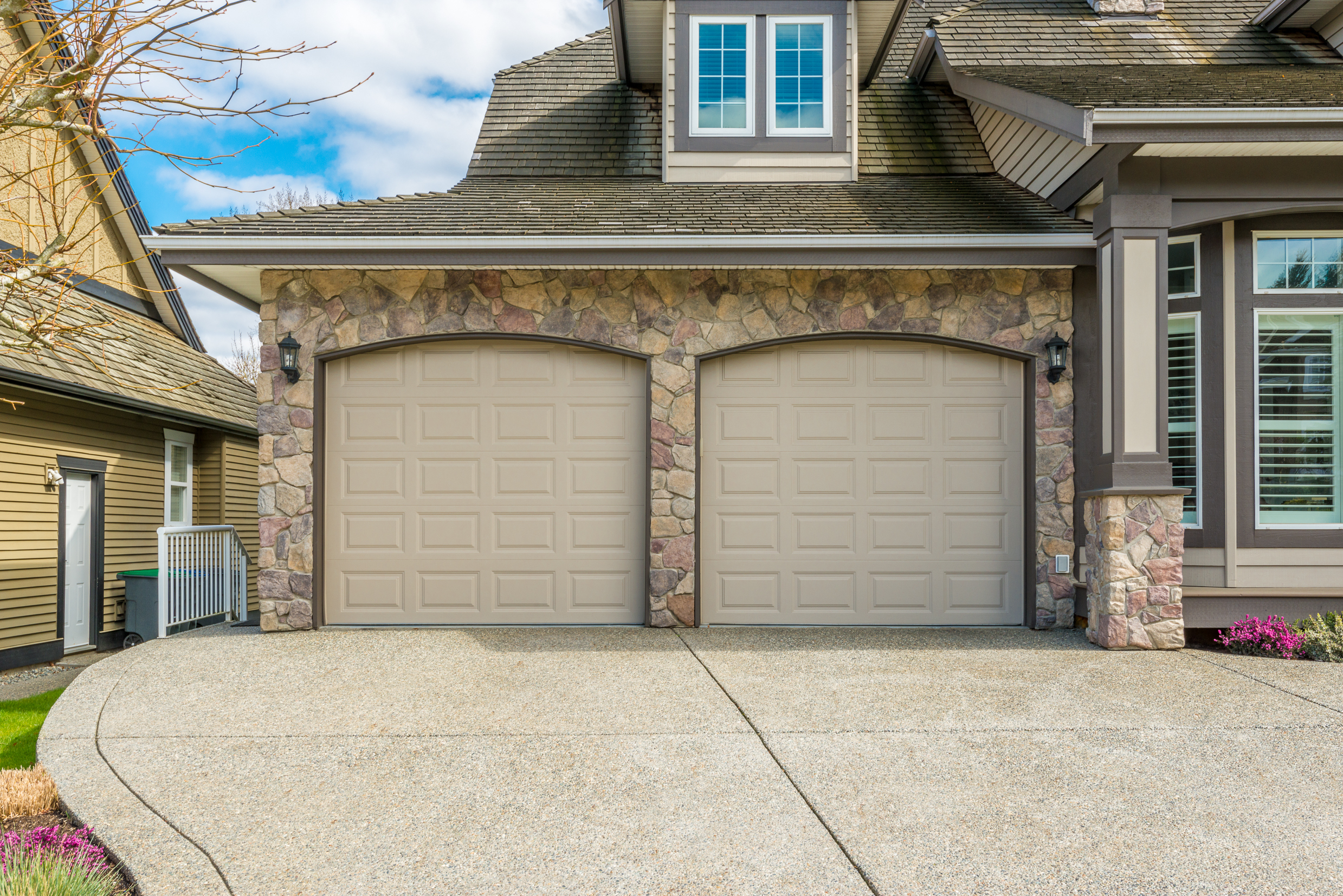 Two-car garage attached to large house with stone siding.