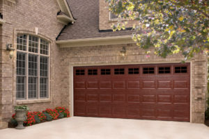 Maroon two-car raise-panel garage door with small windows across the top, in a tan brick home.