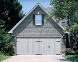 White two-car garage door on a large gray brick home with trees surrounding.