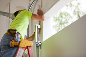 Technician repairing a garage door while standing on a ladder.